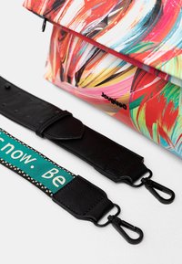 Kolorowa torba w wzory o gładkim, błyszczącym wykończeniu; posiada odpinany czarny pasek z ekoskóry z tkanym paskiem w odcieniach teal i białym.