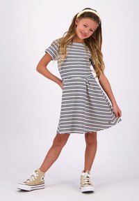 Gestreiftes Kleid in Marineblau und Weiß, kurze Ärmel, ausgestellter Rock, kombiniert mit beigen High-Top-Sneakern, akzentuiert durch ein Logodetail.