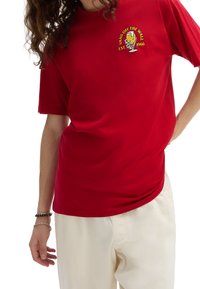 Camiseta de algodón roja con mangas cortas y escote redondo, que presenta un logo gráfico amarillo con la inscripción "Vans Off The Wall" en el pecho.