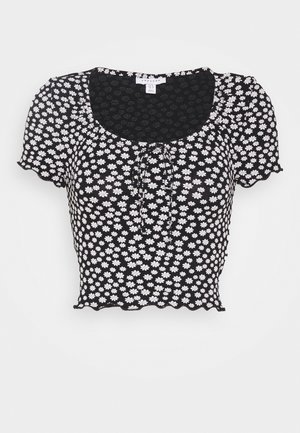 Zwarte cropped blouse met korte pofmouwen, witte madeliefprint, ronde halslijn, detail met strik aan de voorkant en een rand met kroeshaar aan zoom en manchetten.