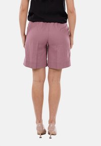 Shorts rosa chiaro con vestibilità rilassata, realizzati in un tessuto morbido. Presentano una vita alta e un orlo fino al ginocchio, abbinati a tacchi alti color nude.