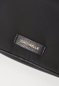 Borsa nera in nylon con etichetta in pelle nera testurizzata e marchio dorato. Superficie liscia con dettagli imbottiti lungo i bordi.