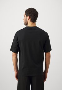 Camiseta de algodón negra con un corte relajado, mangas cortas y cuello redondo. Textura suave, sin patrones visibles ni detalles de hardware.