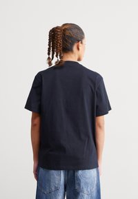 Sort kortærmet t-shirt med rund hals, lavet af bomuld. Båret med lyseblå denim jeans med logo-detalje på lommen.