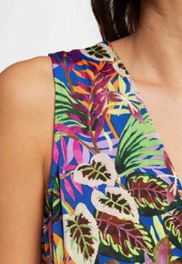 Blusa sin mangas colorida con un fondo azul y patrones vibrantes de hojas en verde, rosa y púrpura. Textura de tela suave.