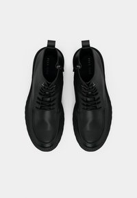 Černé kotníkové boty s hladkým koženým povrchem, kulatou špičkou, šněrováním v přední části a dvojitými poutky pro snadné nazouvání. Texturovaná gumová podrážka.