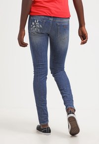 Kapeat siniset farkut, joissa on haalistuneet alueet, brodeerattu takataskudesign ja keskikorkea vyötärö. Yhdistetty mustiin lenkkikenkkiin.