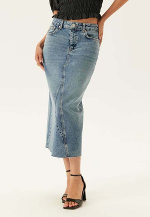 Kvinna som bär en midjehög, ljusblå denim-midlång kjol med frontslits, kombinerad med svarta högklackade sandaler med ankelrem.