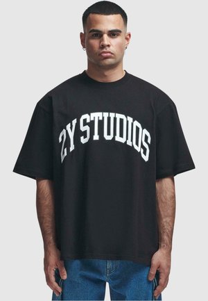 Black cotton t-shirt with oversized fit, featuring white "ZY STUDIOS" text in an arched design across the chest. Short sleeves, crew neck.