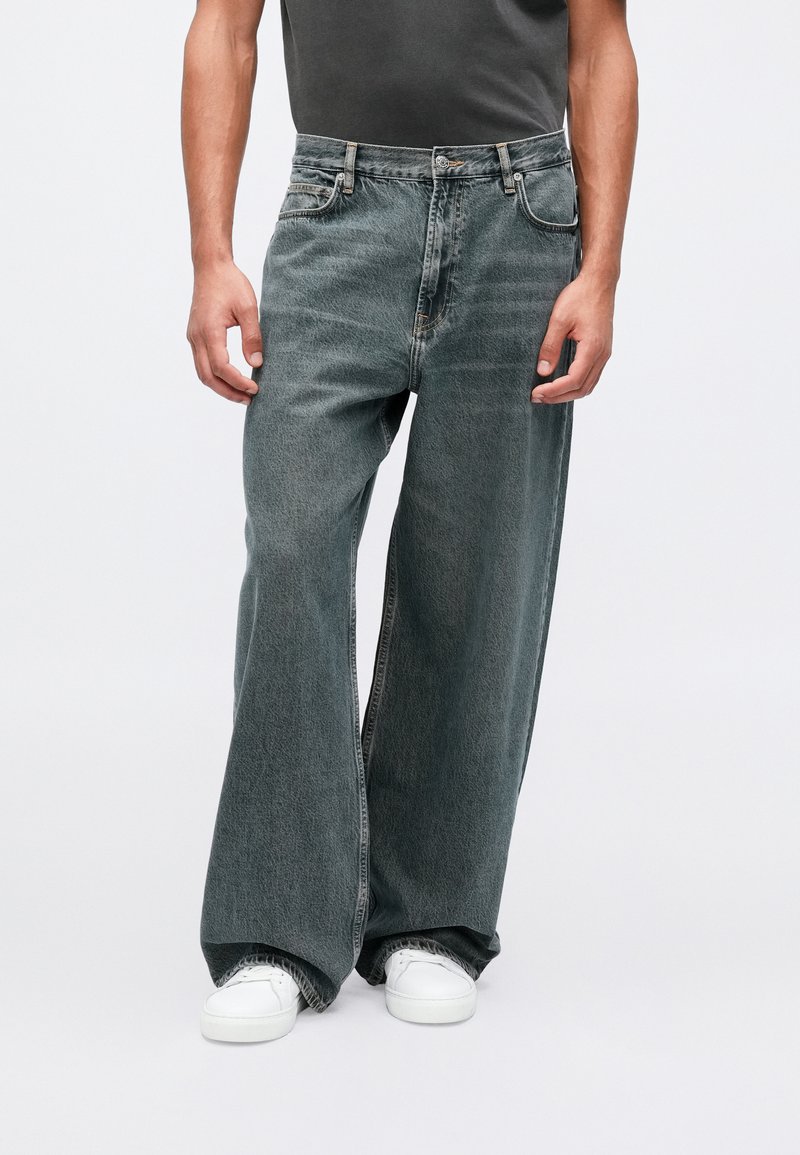 Jeans de pierna ancha en denim gris desgastado con un acabado texturizado, con un diseño clásico de cinco bolsillos y costuras en la cinturilla.