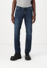 Dark blue denim jeans with a straight leg fit, subtle fading, five-pocket design, and contrast stitching. Paired with black lace-up boots.