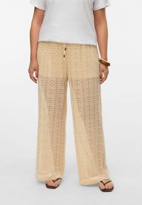 Beige heklet brede bukser med et cirkulært mønster, der har en elastisk talje og snor med trædetaljer.