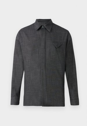 Harmaa, pitkähihaisessa paidassa on tekstuurikangasta. Siinä on terävä kaulus ja pieni rintatasku, jossa on kolmiomainen läppä.