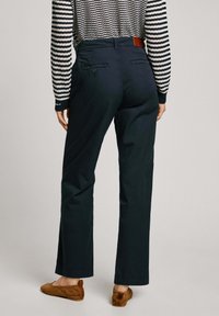 Pantalones rectos de color azul marino, confeccionados en una tela suave, con dos bolsillos traseros y una etiqueta de cuero marrón en la cinturilla.