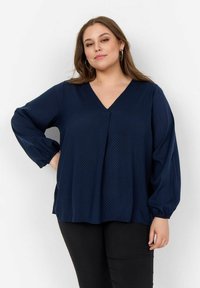 Marinebluse mit V-Ausschnitt, langen Puffärmeln und subtilen Punkten. Aus leichten Stoff hergestellt, lässige Passform.