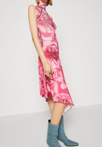 Bezramienna, różowa sukienka w kwiaty z wysokim kołnierzem i falbaną u dołu, uszyta z miękkiego materiału. W zestawieniu z jasnoniebieskimi botkami do kostki.