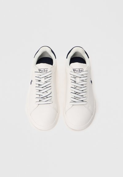 Ténis brancos com parte superior sintética lisa, detalhes em azul-marinho na língua e no logótipo, com atacadores redondos e sola texturizada.