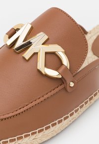 Chaussure espadrille en cuir marron avec boucle décorative métallique dorée et détail de couture visible sur la semelle en jute tissée.