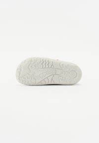 Hvit gummisåle med teksturerte gripe mønstre og "Frodo Barefoot" logo. Reflekterer et minimalistisk design og slitesterkt materiale.