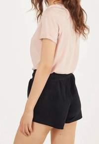 T-shirt en coton rose clair avec des manches retroussées, associée à un short en tissu noir doux avec une taille élastique.