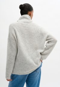 Light gray oversized sweater with a ribbed turtleneck, textured knit, and dropped shoulders, paired with high-waisted blue denim jeans.