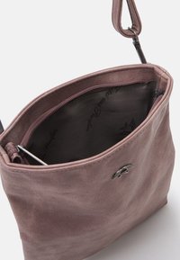 Rosa läderhandväska med en dragkedja på toppen och en mjuk yta. Inuti är den fodrad med mörk tyg som har ett subtilt mönster.