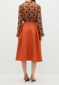 Långärmad blus med ett abstrakt mönster i brunt, orange och off-white; matchad med en knälång orange kjol med veck.