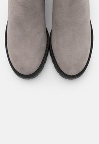Botines de ante gris hasta el tobillo con punta redondeada y suelas de goma negra. La textura es suave, con costuras visibles a lo largo de los bordes.
