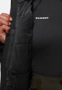 Schwarze Pufferjacke mit einer Reißverschlusstasche und einem matten Innenfutter. Die innere Schicht ist schwarz und wird von einem Logo akzentuiert.