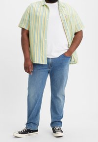 Kortärmad randig skjorta i ljusgrön, gul och blå, över en vit T-shirt. Bärs med blå jeans och svarta sneakers.