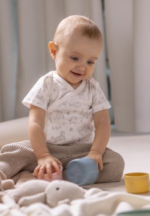Helles graues Kurzarmhemd mit Tiermotiven, beiger gerippter Hose, sitzt auf einer weißen Oberfläche, umgeben von Kuscheltieren und bunten Tassen.