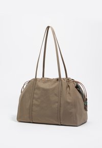 Bolsa de tela de color topo con asas largas, parte superior fruncida y detalles decorativos de cuero y tejido. Textura suave y diseño de gran tamaño.