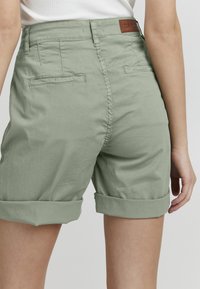 Shorts en coton vert clair avec des revers, dotés de poches arrière et d'une étiquette de marque en cuir à la taille.