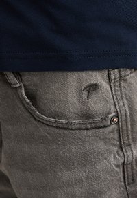 Grijze denim jeans met een gestructureerde afwerking, voorzien van een klein geborduurd logo op de achterzak en een metalen knoopdetail.