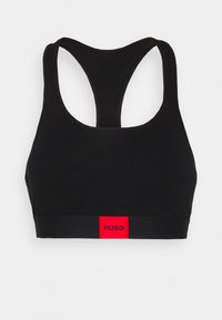 Čierny športový top vyrobený z mäkkého, elastického materiálu. Disponuje strihom s prekríženými ramienkami a červeným logom na spodnej strane pre kontrast.