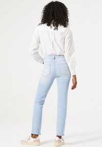 Jeans de mezclilla azul claro con un corte ajustado, combinados con una camisa blanca de botones. Presentan bolsillos traseros y detalles de costura mínimos.