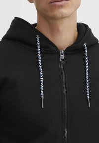 Čierna mikina na zips s textúrovanou tkaninou, s opaskami v modro-bielej farbe a detailom so strieborným zipsom.