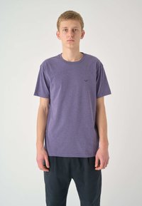 Kurzärmeliges lila T-Shirt aus weichem Stoff mit Rundhalsausschnitt und kleinem Logo auf der Brust, kombiniert mit dunklen, lockeren Hosen.
