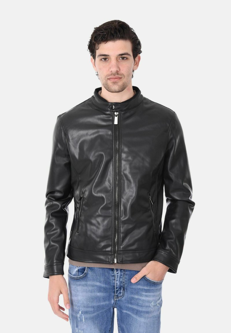 Giubbotto in finta pelle nera con colletto a scatto, chiusura con zip, due tasche laterali e una texture liscia. Indossato sopra una maglietta di colore chiaro.