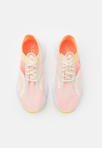 Lehké atletické boty s vrchní částí z růžové a krémové síťoviny, bílou podrážkou a žlutými akcenty. Obsahují podšívku s polstrováním a design na šněrování.