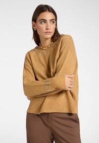Maglione a maglia senape con orlo e polsini a costine, caratterizzato da paillettes decorative lungo il collo e sui dettagli delle maniche.