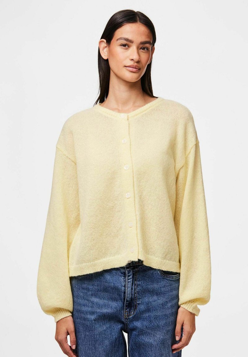 Rumena pletena jopica z okroglim izrezom, dolgimi balonastimi rokavi in zapiranjem na gumb spredaj. Tkanina ima mehak, strukturiran videz.