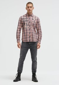 Gestreifte Langarmhemd in Pink und Blau, mit grafischem Text auf der Vorderseite, kombiniert mit enganliegenden grauen Jeans und schwarzen Schnürstiefeln.