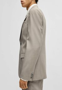 Completo grigio in tessuto strutturato, design monopetto, rever a dischi e polsini con tre bottoni, esposto di lato.