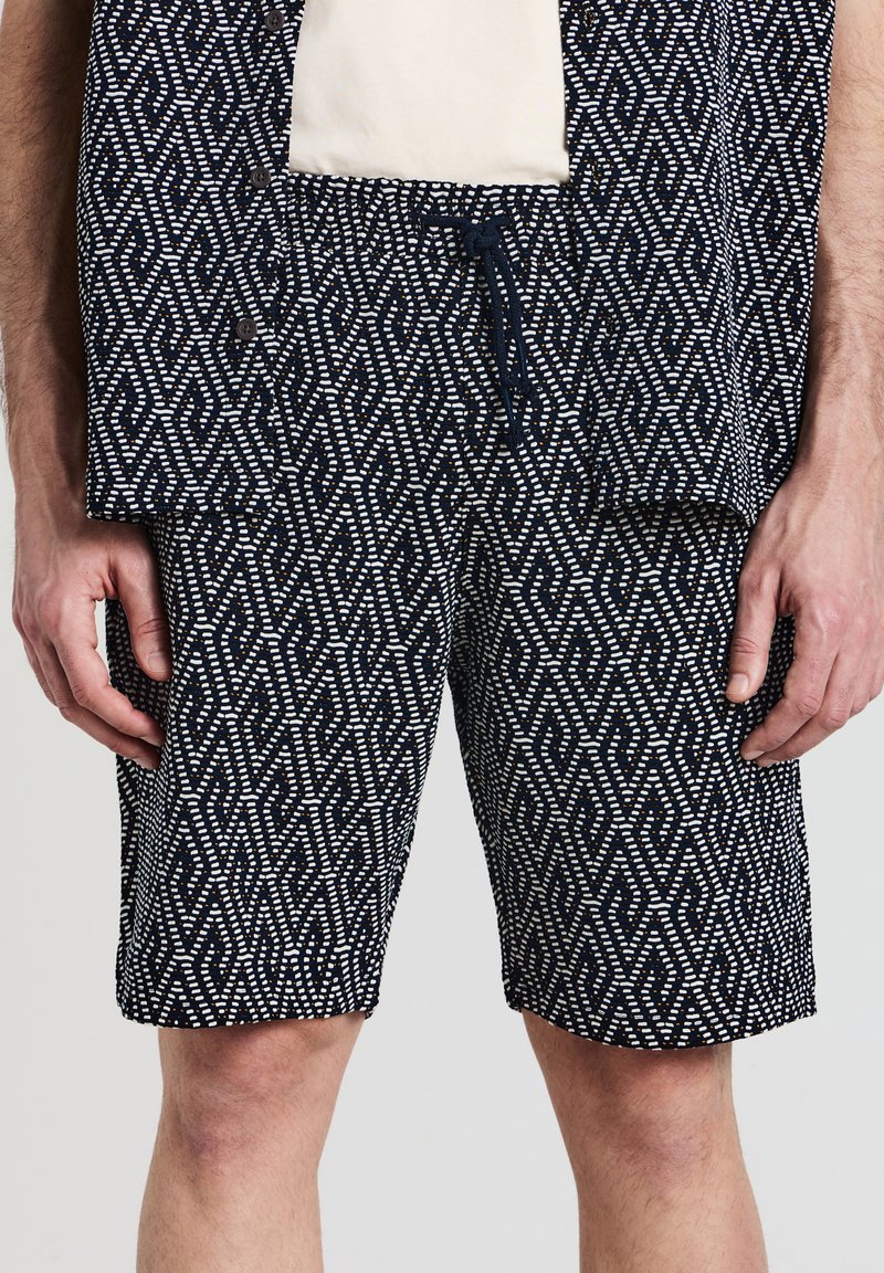 Pantaloni corti blu navy con un motivo geometrico bianco e arancione. Presentano una vita elasticizzata con cordino e tasche laterali. Materiale in cotone.