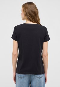 Czarny t-shirt z krótkim rękawem, okrągłym dekoltem, luźny krój, wykonany z miękkiej bawełny, zestawiony z jasnoniebieskimi dżinsami.