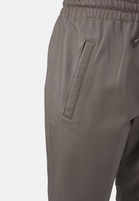 Šedé kožené jogger kalhoty s elastickým pasem a elegantními bočními kapsami. Hladký povrch s jemnými detaily v prošívání.