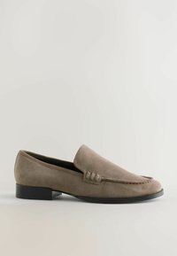 Mocassin en suède marron clair avec un faible talon noir et des coutures sur le dessus, présenté en profil sur un fond uni.