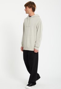 Lys grå hættetrøje med en frontlomme, snøre i hætten og ribbede manchetter. Sæt sammen med løse sorte bukser og sorte sneakers.