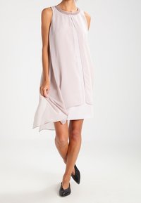 Robe sans manches en tissu rose clair au toucher lisse, avec un col rond orné et une coupe ample et fluide.